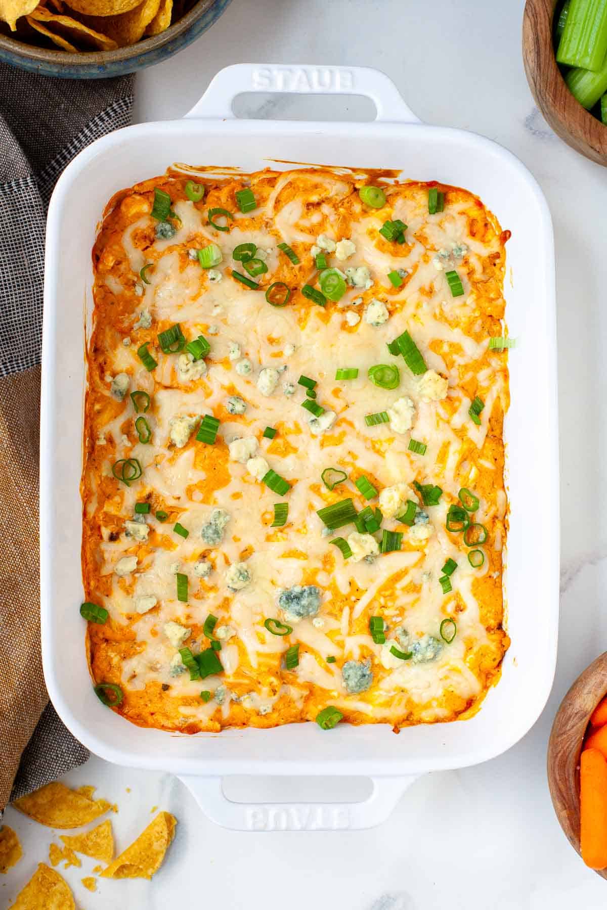 Buffalo Cauliflower Dip in white baking dish topped with sliced green onions and crumbled blue cheese.